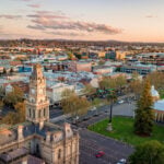 An aerial view of a bustling city center at sunset, featuring a grand historic building with a prominent clock tower