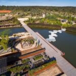 An aerial view of a botanical garden featuring a long pedestrian bridge crossing over a blue lake