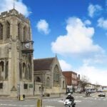 A view of a historic stone church with a tall clock tower on a street corner