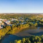 An aerial view of a town situated along a riverbank with dense green trees