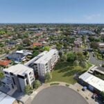 An aerial view of a quiet suburban neighbourhood featuring a modern, multi-storey white apartment complex