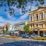 A street-level view of a sunny city street lined with a mix of historic and modern buildings