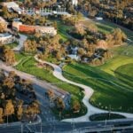 An aerial view of a sprawling green park with a winding white pedestrian path