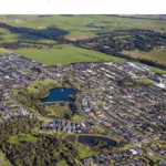 An expansive aerial view of a sprawling suburban residential area bordering lush green farmlands