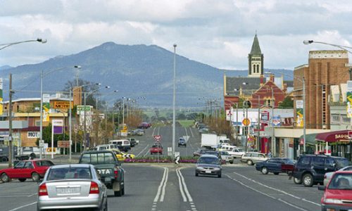 A view from the center of a wide road looking toward a distant mountain peak under an overcast sky.