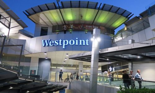 A view of the modern "Westpoint" shopping center entrance at twilight, featuring illuminated blue signage and tiered architectural levels.