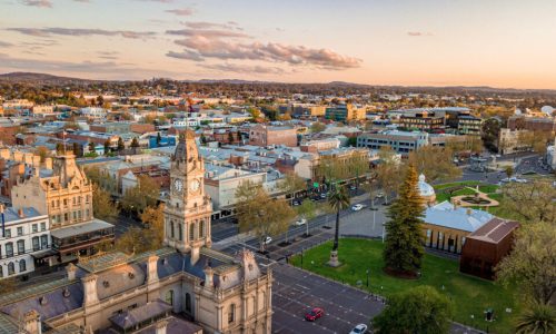 An aerial view of a sprawling town at sunset, featuring a prominent historic clock tower in the foreground.