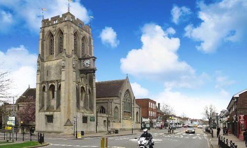 A view of a historic, grey stone church with a square tower and a prominent external clock