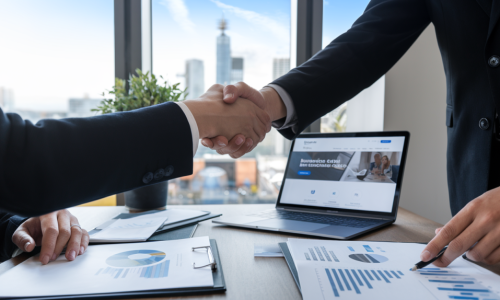 A close-up of two people in dark business suits shaking hands over a wooden desk.