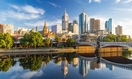 A wide shot of a modern city skyline reflected in the calm surface of a river