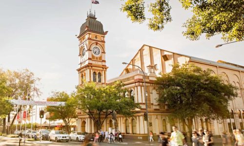 Norwood street-level view of a grand historic building with a prominent tiered clock tower under a clear sky.