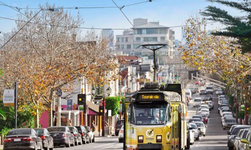A yellow tram labeled "Toorak via" travels down a busy city street lined