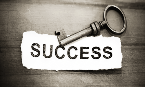 an antique metal key resting on a piece of torn white paper with the word "SUCCESS"