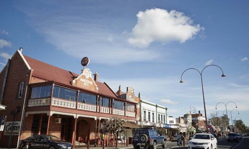A ground-level view of a wide town street featuring the historic two-storey brick Grand Central Hotel with an ornate white balcony.